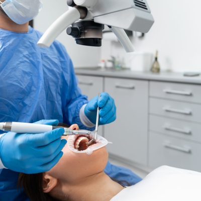 A young European male dentist treats a patient's teeth using a modern microscope.
